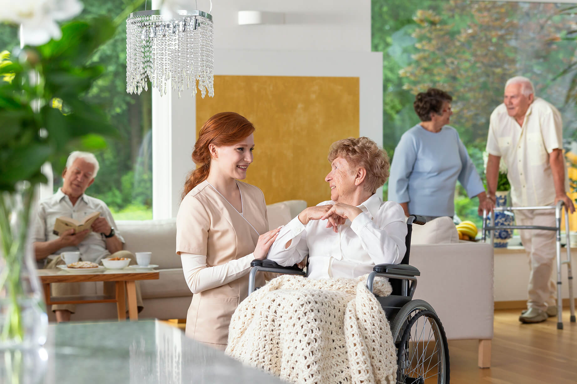 Pflegekraft unterhält sich mit Seniorin im Rollstuhl